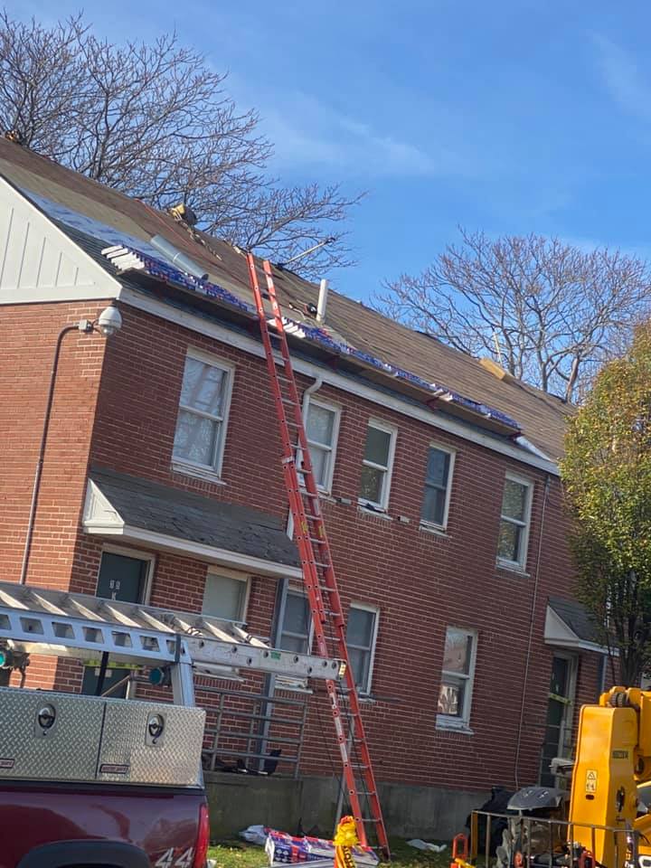 Roofing installation in progress with red ladder up against brick building