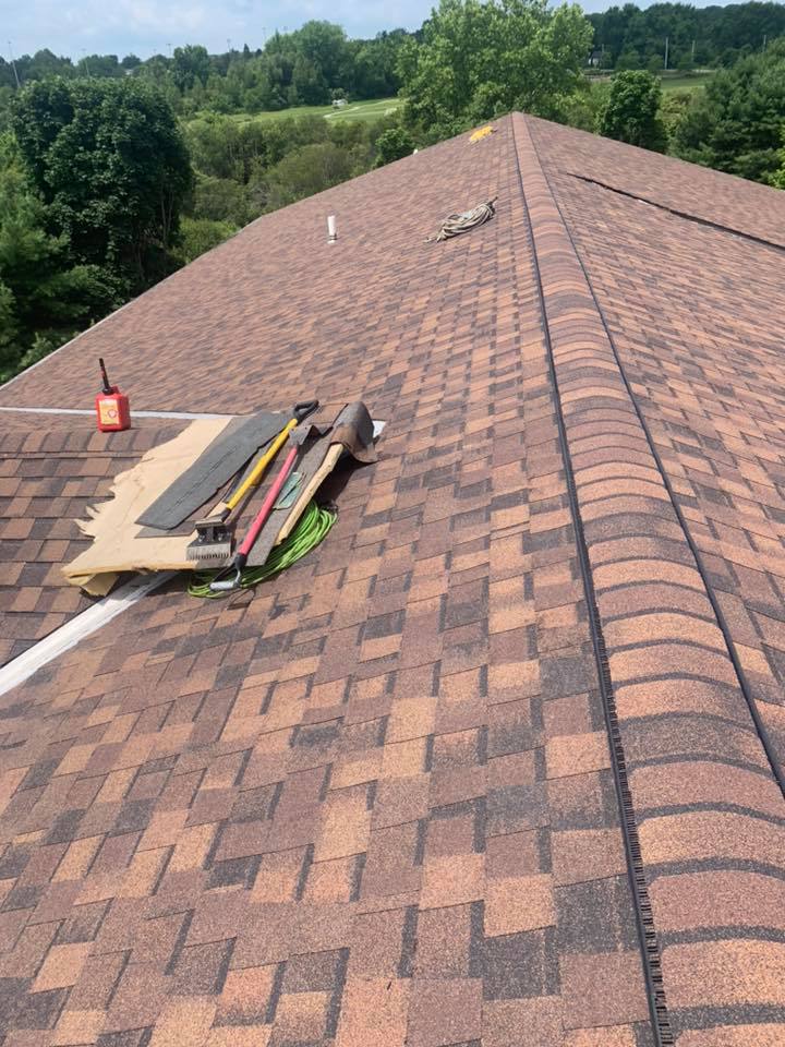 Installing brown asphalt shingles on round roof process with brown surface with tools sitting on top of roof