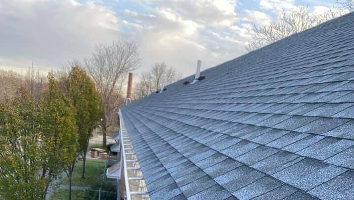 Newly installed gray asphalt roofing with view of cloudy sky and tree line
