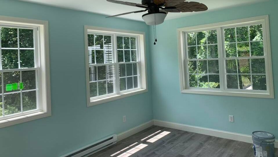 Newly remodeled one room addition with three large windows with white trim, gray wood like flooring and blue walls